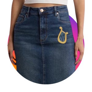 Può includere: Gonna di jeans di media tonalità con un classico design a cinque tasche. La gonna presenta una toppa a forma di arpa ricamata color oro sul davanti. La gonna ha una chiusura con bottone e cerniera e passanti per cintura.