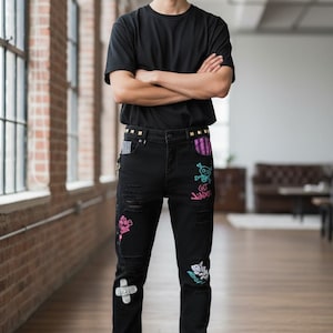 May include: Black denim jeans with distressed details and colorful graffiti-style patches. The jeans feature a studded belt and are paired with a black t-shirt and white sneakers. The overall style is urban and edgy.