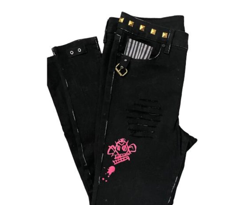Puede incluir: Vaqueros negros con detalles desgastados, con un gr&aacute;fico rosa y tachuelas doradas en la cintura. Los vaqueros tienen un forro de bolsillo a rayas y un cierre de hebilla.