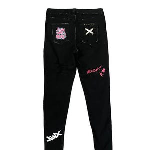 Puede incluir: Pantalones vaqueros negros con textos y dise&ntilde;os de estilo graffiti en blanco y rosa. Los bolsillos traseros presentan un dise&ntilde;o de "X" y un gr&aacute;fico rosa y blanco. La palabra "Jinx" est&aacute; escrita en blanco en la parte inferior izquierda de la pierna.
