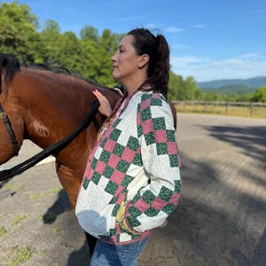 May include: A quilted jacket with a patchwork design featuring pink and green squares on a white background. The jacket has a relaxed fit and is worn with blue jeans. The sleeves and hem are trimmed with a yellow floral fabric.