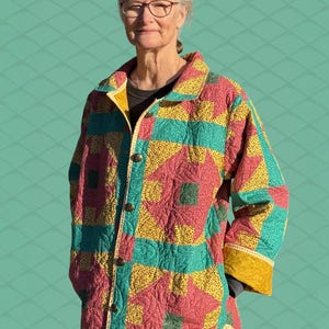 May include: A quilted jacket with a colorful patchwork design. The jacket features a mix of red, yellow, and teal squares and geometric patterns. It has a collared neckline, button closure, and yellow trim along the cuffs and hem. The jacket is worn by a person.
