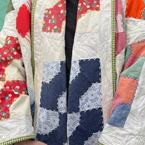 Peut inclure: Veste patchwork avec une variété de motifs et de couleurs de tissus. La veste présente des sections florales rouges, florales bleues et matelassées blanches unies. Une bordure en vichy vert borde la veste.