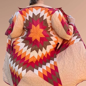 May include: A quilted coat featuring a starburst pattern in shades of orange, red, brown, and cream. The coat has a quilted design and a collar. The coat is open, revealing the lining and the intricate stitching.