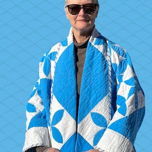 Peut inclure: Veste matelassée à motifs bleus et blancs. Le motif géométrique présente des losanges bleus et des motifs floraux blancs. La veste est portée ouverte, révélant les vêtements du porteur. Une pièce de vêtement unique.