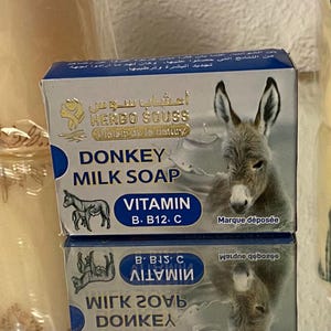 May include: A box of Donkey Milk Soap with a picture of a donkey. The box has the words "DONKEY MILK SOAP" and "VITAMIN B, B12, C" printed on it. The brand name "HERBO SOUSS" is also visible.