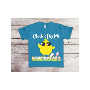 May include: A turquoise blue t-shirt with a yellow chick wearing sunglasses and the text "Chicks Dig Me". The chick is standing on a bed of green grass with colorful Easter eggs.