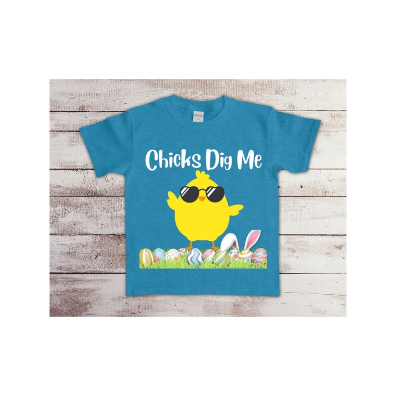 May include: A turquoise blue t-shirt with a yellow chick wearing sunglasses and the text "Chicks Dig Me". The chick is standing on a bed of green grass with colorful Easter eggs.