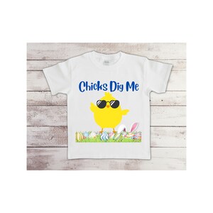 May include: White t-shirt with a yellow chick wearing sunglasses and the text "Chicks Dig Me". The chick is standing on a bed of green grass with colorful Easter eggs.