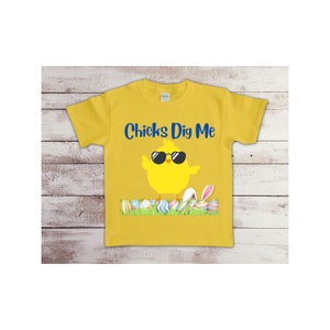 May include: Yellow t-shirt with a cartoon chick wearing sunglasses and the text "Chicks Dig Me". The chick is standing on a bed of green grass with colorful Easter eggs.