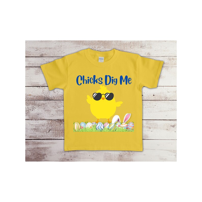 May include: Yellow t-shirt with a cartoon chick wearing sunglasses and the text "Chicks Dig Me". The chick is standing on a bed of green grass with colorful Easter eggs.