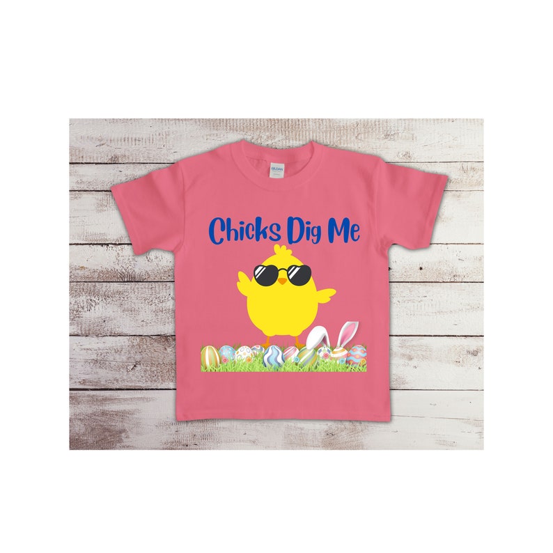May include: Pink t-shirt with a yellow chick wearing sunglasses and the text "Chicks Dig Me". The chick is standing on a bed of green grass with colorful Easter eggs.