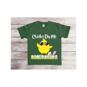May include: A green t-shirt with a yellow chick wearing sunglasses and the text "Chicks Dig Me". The chick is standing on a bed of green grass with colorful Easter eggs.