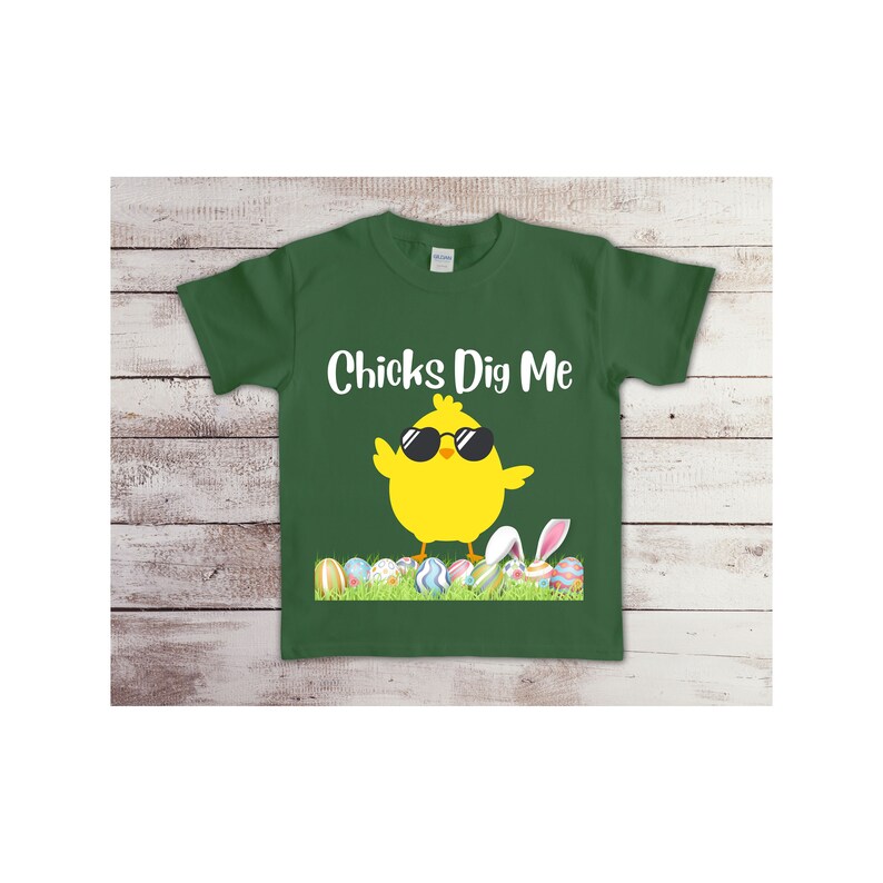 May include: A green t-shirt with a yellow chick wearing sunglasses and the text "Chicks Dig Me". The chick is standing on a bed of green grass with colorful Easter eggs.