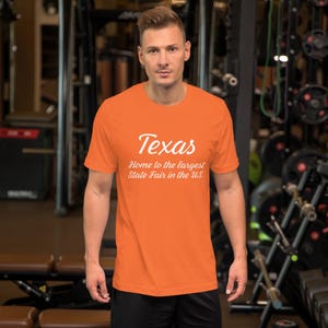 May include: Orange short-sleeved t-shirt with white text that reads "Texas Home to the largest State Fair in the U.S."