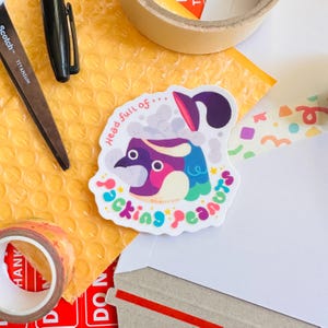 May include: A colorful sticker with a cartoon penguin wearing a purple and white hat with a blue and green scarf. The penguin is in a bathtub with bubbles and the text "Head full of... Sucking Peanuts" is written around the penguin.