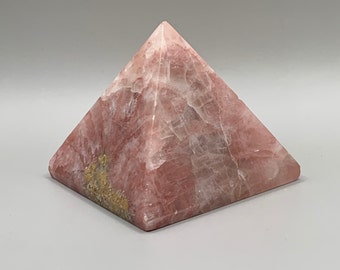 Op de afbeelding: Een roze en witte kristallen piramide met een gouden gevlekt patroon.