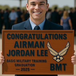 May include: A smiling person in a blue uniform holds a wooden plaque. The plaque reads "CONGRATULATIONS AIRMAN JORDAN LEE BASIC MILITARY TRAINING GRADUATION - 2025 - BMT" with an emblem.