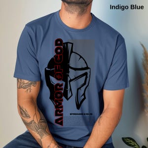 Puede incluir: Camiseta azul índigo con un gráfico negro y rojo de un casco espartano. Las palabras "ARMOR OF GOD" están impresas verticalmente en el lado izquierdo. El texto "EPHESIANS 6:10-18" está impreso debajo.