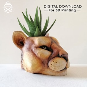 Puede incluir: Una maceta con forma de cabeza de león pintada a mano con una planta suculenta. La maceta es una descarga digital para impresión 3D. La cara del león es marrón y beige, con hojas verdes. El texto "DESCARGA DIGITAL - Para impresión 3D" está en la parte superior.