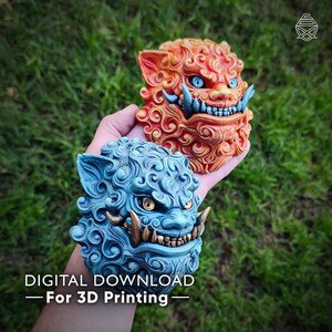 Puede incluir: Dos esculturas detalladas de perros león, una naranja y otra azul, con intrincadas melenas rizadas y expresiones feroces. Las esculturas tienen ojos azules y dientes dorados. El texto en la parte inferior dice "DESCARGA DIGITAL - Para impresión 3D".