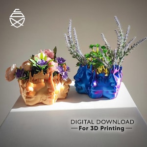May include: Two decorative face planters, one gold and one blue, each filled with flowers and greenery. The gold planter holds pink and purple flowers, while the blue one features lavender and green plants. Text at the bottom reads "DIGITAL DOWNLOAD - For 3D Printing".