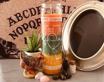 May include: A multi-colored candle with the words "ABRE CAMINO" and "ROAD OPENER" is displayed. The candle is next to a decorative frame, a ceramic chicken figurine, a small succulent, and several crystals and small bottles.