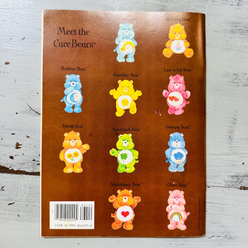Peut inclure: Une couverture de livre vintage avec les Bisounours. La couverture est marron avec des illustrations de divers Bisounours de diff&eacute;rentes couleurs, chacun avec un symbole unique sur le ventre. Le texte comprend "Meet the Care Bears" et les noms des ours.
