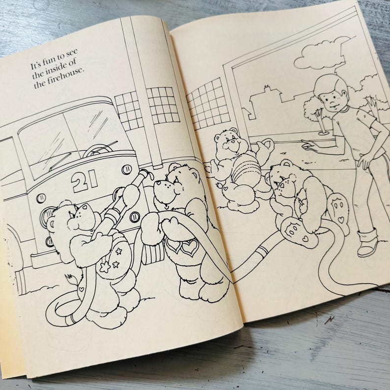 Peut inclure: Un livre ouvert avec une illustration en noir et blanc d'oursons c&acirc;lins dans une caserne de pompiers. Le camion de pompiers porte le num&eacute;ro 21. Le texte dit : "C'est amusant de voir l'int&eacute;rieur de la caserne."