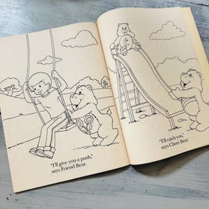 Peut inclure: Livre ouvert avec des illustrations de Bisounours. Une image montre un gar&ccedil;on sur une balan&ccedil;oire avec Grosch&eacute;ri. L'autre montre un Bisounours sur un toboggan avec Grosjojo. Le texte comprend "Je vais te pousser" et "Je vais t'attraper."
