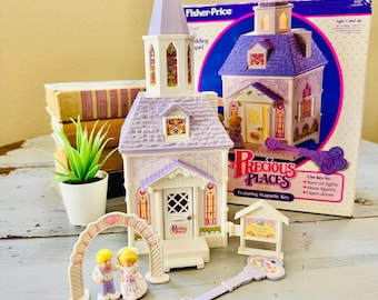 Può includere: Un playset della cappella nuziale Fisher-Price Precious Places. Il set include una cappella bianca e viola, una statuina di sposi, un arco e una chiave. La scatola recita "Ages 5 and up" e "Featuring Magnetic Key".