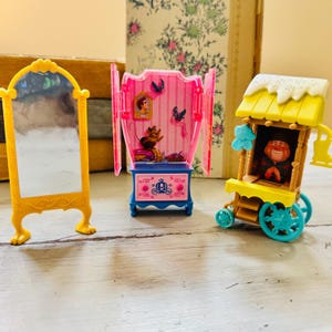 May include: A yellow decorative mirror, a pink and blue miniature cabinet with Cinderella figures, and a yellow and blue toy wagon with a character inside. The toys are on a light-colored surface.