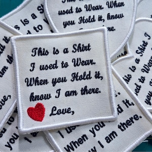 May include: A square white fabric patch with black embroidered text that reads: This is a Shirt I used to Wear. When you Hold it, know I am there. Love, and a small red embroidered heart at the bottom left corner.