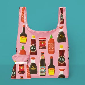 Puede incluir: Bolsa de compras reutilizable rosa con un estampado de varias salsas y condimentos asiáticos. La bolsa incluye una bolsa a juego. Las salsas están en botellas y frascos de diferentes formas y tamaños, con etiquetas coloridas.