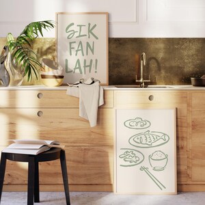 Puede incluir: Dos impresiones enmarcadas en un ambiente de cocina. La impresi&oacute;n superior tiene el texto "SIK FAN LAH!" en escritura verde. La impresi&oacute;n inferior presenta un dibujo de l&iacute;nea verde de un plato de comida con pescado, arroz y palillos.