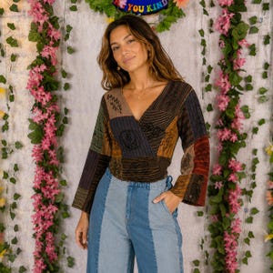 May include: A long-sleeve wrap top featuring a patchwork design with various earth-toned panels in brown, black, and rust, accented by black line-art graphics, paired with high-waisted blue denim jeans constructed from two different shades of blue.