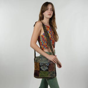 May include: A patchwork shoulder bag with a bear design, featuring squares of brown, green, and blue fabric. The bag has a long strap and is worn over the shoulder. The person is wearing a colorful crochet top and green pants.