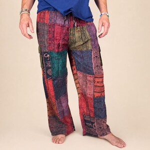 May include: Loose-fitting patchwork trousers featuring a vibrant mix of red, blue, green, and purple fabric panels. The pants are decorated with repeating black printed symbols and circular motifs, including an elastic waistband and side cargo pockets.