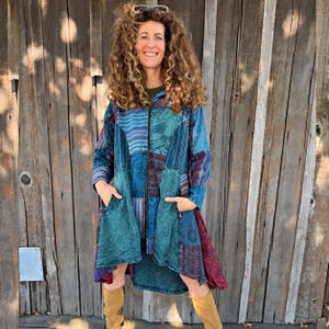 May include: A long-sleeved, zip-up jacket featuring a patchwork design in various shades of blue, teal, and maroon. The garment includes a high-low hemline, two front pockets, and a hood, constructed from multiple patterned fabric panels.