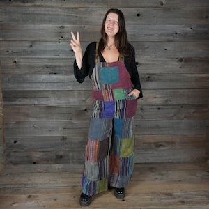May include: A woman wearing a patchwork overall dress with a variety of colours, including purple, blue, green, and brown. The dress has a wide leg and is made of a soft, comfortable fabric.