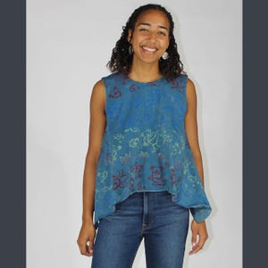 May include: A sleeveless blue top with a bear design in red, yellow, and blue. The top is paired with blue jeans. The top has a unique, flowing shape.