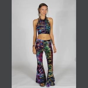 May include: A woman wearing a tie-dye halter top and matching bell bottom pants. The top and pants have a geometric pattern in shades of purple, blue, green, and black.