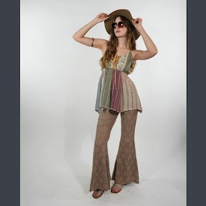 Könnte beinhalten: Eine Frau trägt einen braunen Hut, eine Sonnenbrille und ein bunt gestreiftes Oberteil. Sie trägt auch eine braune Schlaghose aus Spitze und Sandalen. Das Outfit hat einen böhmischen, Retro-Stil.