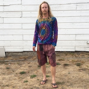 May include: A person wearing a long-sleeved tie-dye shirt with a colorful mandala design. They are also wearing patchwork cargo shorts and brown sandals.