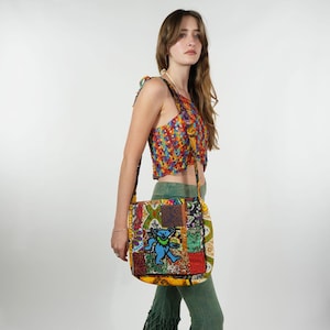 May include: A patchwork shoulder bag with a blue dancing bear motif. The bag incorporates various patterned fabrics in red, yellow, green, and blue. The strap is black. The person is wearing a matching patchwork crop top and green trousers.