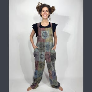 May include: Multi-colored patchwork overalls with black graphic designs. The overalls have a bib front with adjustable straps and pockets. The garment is made of a woven fabric and features a variety of colors including red, green, blue, and gray.