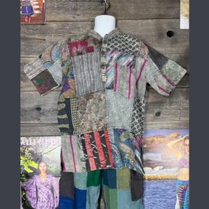 May include: A short-sleeved patchwork shirt in various colours and patterns, including floral and striped designs. The shirt has a mandarin collar and a button-down front. The garment is displayed on a white mannequin.