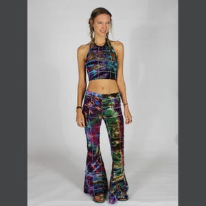 Puede incluir: Una mujer lleva un top halter de tie-dye y pantalones acampanados a juego. El top y los pantalones tienen un patrón geométrico en tonos de morado, azul, verde y negro.