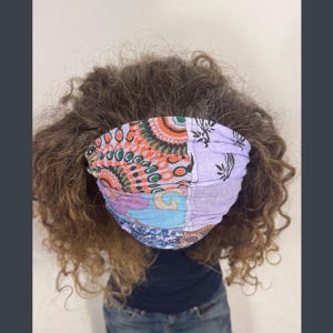 May include: A colorful patchwork headband with orange, purple, and blue patterns. The fabric is soft and appears to be cotton. The headband is worn on the head and is a stylish accessory.