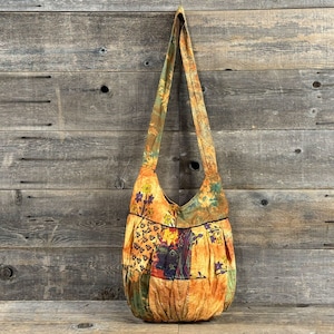 Op de afbeelding: Een patchwork-schoudertas met een bloemenprint in tinten oranje, geel, groen en bruin. De tas heeft een lange schouderband en een gerimpeld ontwerp.